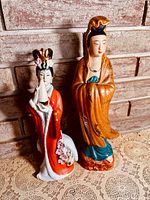 Both porcelain figurines side by side on lace cloth, brick background