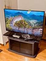 Front view of Sony TV on stand with screen on, showing overall condition and included accessories (remote, cables)