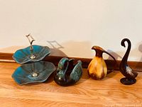 Photo showing all four Blue Mountain Pottery pieces: two-tier dessert plate stand, two swan figurines, and one pitcher/jug.