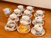 View of 10 assorted vintage fine bone china tea cups and matching saucers arranged on a wooden surface, showing various floral and bird designs.