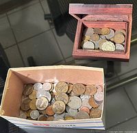 Two boxes filled with assorted international coins showing various sizes, materials, and designs