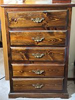 Front view of the wood tallboy dresser showing five drawers and brass handles.