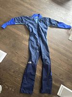 Full view of blue Bev skydiving suit laid out flat on wooden floor, showing overall design and condition