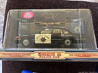 Full side view of black and white Code 3 police car model in clear plastic case with California Highway Patrol markings visible.