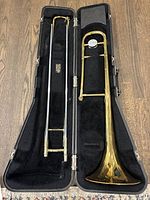 Brass trombone and black velvet-lined hard case fully open showing instrument and case compartments