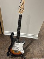 Full view of Peavey Raptor Plus electric guitar with sunburst finish and black strap, standing vertically on floor.