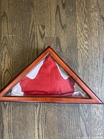 Triangular wooden flag display case with folded Canadian flag inside, displayed on wooden floor