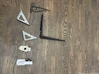All brackets shown laid out on wooden floor including shelf brackets, flagpole brackets, and plant hanger bracket.