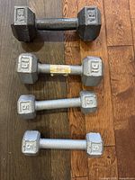 5 dumbbells arranged on wooden floor, showing 2 black 2.5lb, 2 silver 5lb and 1 black 12lb dumbbells.