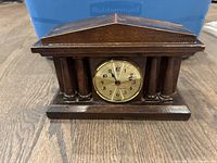 Wooden mantel clock with dark wood finish, classical columns, and round clock face, battery operated.