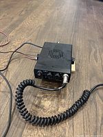 Front angle view of Midland Model 1001ZBlack CB radio with microphone cable attached, sitting on wood floor.