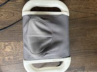 Top view of the electric neck massager showing fabric-covered massage area and white handles on wooden floor