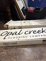 Two unopened boxes of Opal Creek hardwood flooring with company branding visible on the packaging.