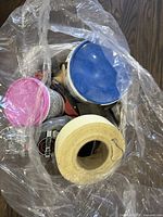 View into the basket showing multiple containers including CGC Sheetrock compound with blue lid, pink container, a roll of drywall tape, and other painting-related items.