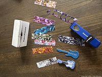 Guitar pick maker kit including punch, multicolored strips, and pick holders laid out on wooden table.