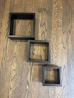Three black square floating shelves arranged on wooden floor showing sizes and color