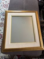 Photo of traditional rectangular mirror with gold frame and fabric border laying on furniture, showing minor wear on frame