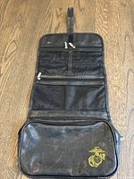 Front view of the dopp kit with multiple zippered mesh pockets and a main black leather pouch with the US Marines emblem.