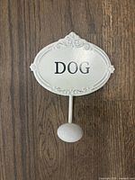 Photo of the white metal wall hook with vintage design, showing the 'DOG' label on the oval plaque and the rounded hook below.