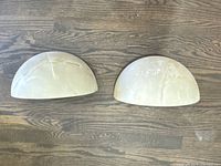 Pair of 2 half moon marble beige wall sconces lying flat on wooden floor, showing entire shape and color.