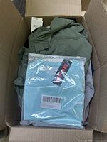 Box with green jacket or shirt and light teal packaged garment visible