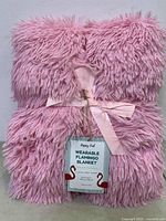 Photo of rolled pink fluffy plush wearable flamingo blanket with a pink ribbon and visible product tag reading 'Wearable Flamingo Blanket'.