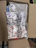 Box containing two sealed Saint Dahlia floral pajama sets with white and colorful floral prints