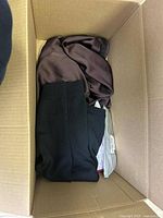 Box of clothes showing silky brown and black knitwear inside a cardboard box.
