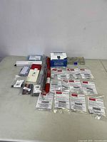 Wide view of all items spread out on table including red heated tube replacement, multiple small packaged hardware items, and plastic case with metal pins.