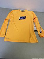 Front view of kids medium Nike long sleeve swim top in yellow with large blue Nike logo on chest and blue Nike swoosh on sleeve cuff.