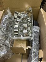Top view of open cardboard box showing metal cookie cutters in plastic container, bubble wrapped cylindrical items, cardboard boxes, and a long wrapped item inside the box.