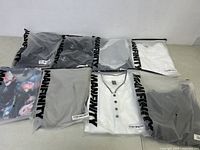 Eight Manfinity branded plastic bags each containing a men's clothing item, laid out on a floor surface to show quantity and packaging.