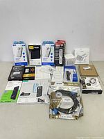 Photo of multiple new electronic accessories and phone accessories in retail packaging on a flat surface.