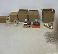 Photo showing five different Christmas ornaments and their original boxes on a white table: two clear glass hanging ornaments, two orange boxed vintage-style round ornaments, a triangular tray of colorful small ball ornaments, and a snowflake ornament in plastic packaging.