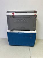 Side view of two coolers stacked, gray IGLOO on top and blue Rubbermaid below, showing external wear and markings.