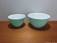 Two aqua blue and white Pyrex mixing bowls side by side on wooden surface, showing size difference and color.