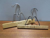 Front view of two Baribocraft wood and metal pants hangers showing wood bars and metal hooks and clamp arms.