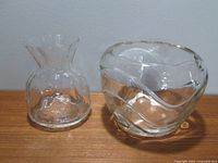 Two clear glass vases side by side showing paper bag style vase on left and round wavy patterned vase on right.
