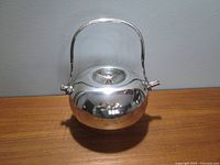 Front view of spherical silver plated teapot with closed lid and upright handle