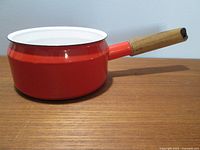 Side view of red enamel sauce pan showing shape, wooden handle, and exterior and interior enamel surfaces