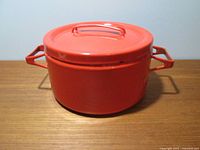 Red enamel stock pot with matching lid. Angular side handles visible. Pot exterior shiny red enamel.
