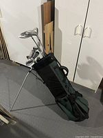 Full view of the black and green golf bag with stand, filled with golf clubs.