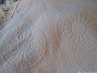 Close-up of the white matelasse fabric showing the detailed Heirloom Heritage pattern with circular and leaf quilted designs.