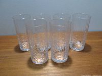 Six tall clear unused glass tumblers with solid bubble pattern positioned in two rows on wooden surface.