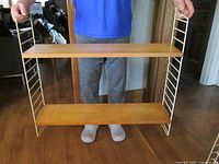 Cream metal ladder frame with two ash veneer shelves held by person