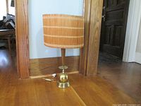 Full view of lamp showing brass-colored metal and wooden base with tall wooden stem and cylindrical shade made of wooden sticks.