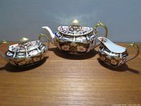 Three-piece tea set: teapot with lid at center, sugar bowl on left and creamer on right on wood surface