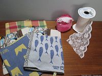 Photo of various cotton and linen tea towels laid out flat along with partial rolls of lace and eyelet trims.