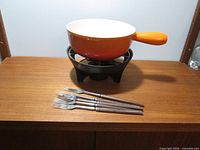 Full view of the Le Creuset fondue pot on cast iron base with removable grill and burner, accompanied by 6 wooden handle fondue forks.