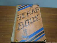 Photo of the exterior of the vintage scrapbook featuring a brown cover with blue and black stripes and multiple scissors illustrations.